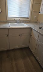 Small kitchen with white cabinets, sink under a window, and light wood flooring.
