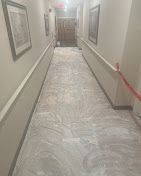 Narrow hallway with white protective floor covering and red tape along the right wall, framed artwork on both sides