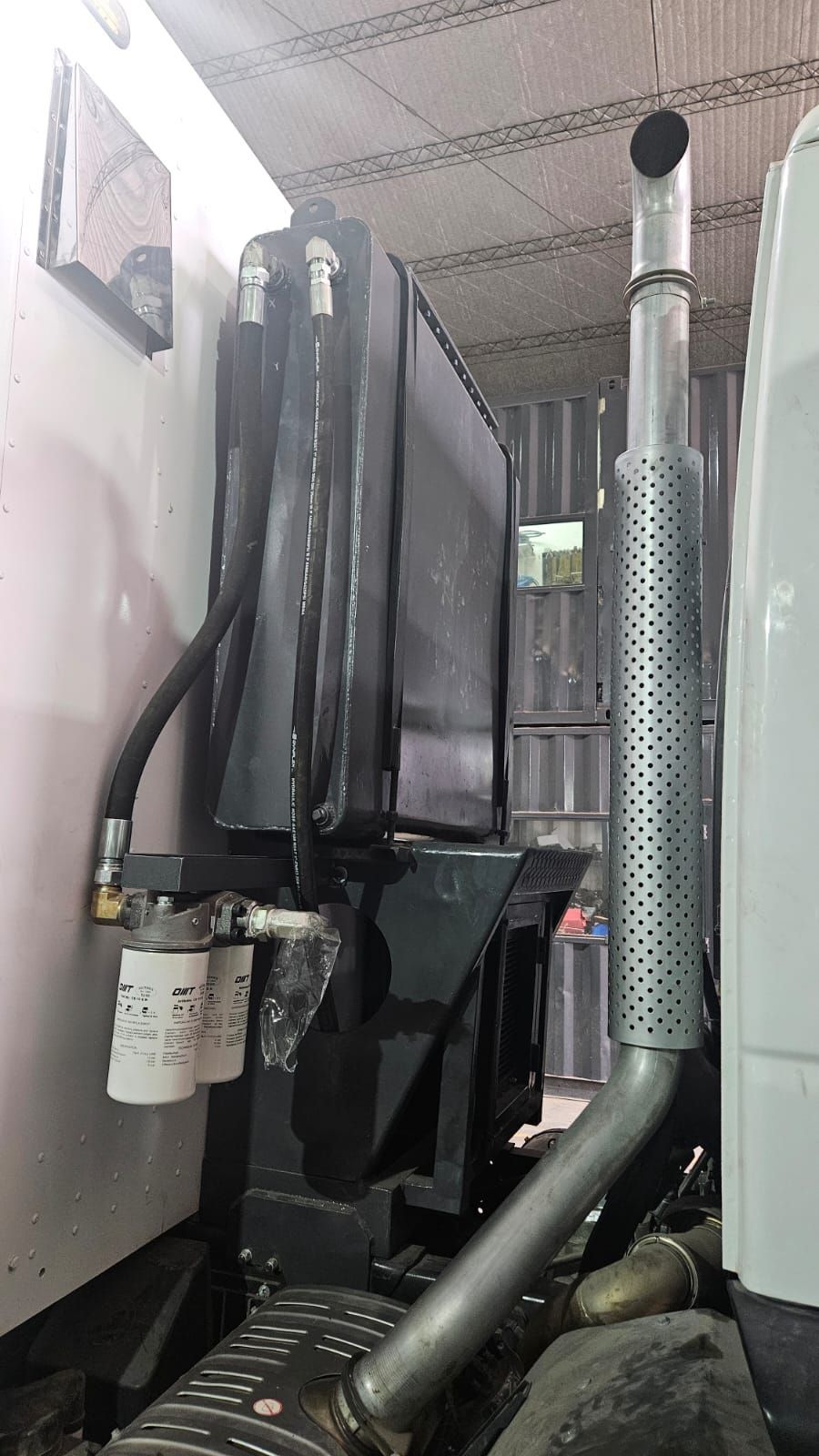 Cuarto de servicio interior con equipos negros apilados y tuberías de ventilación plateadas sobre paredes blancas.