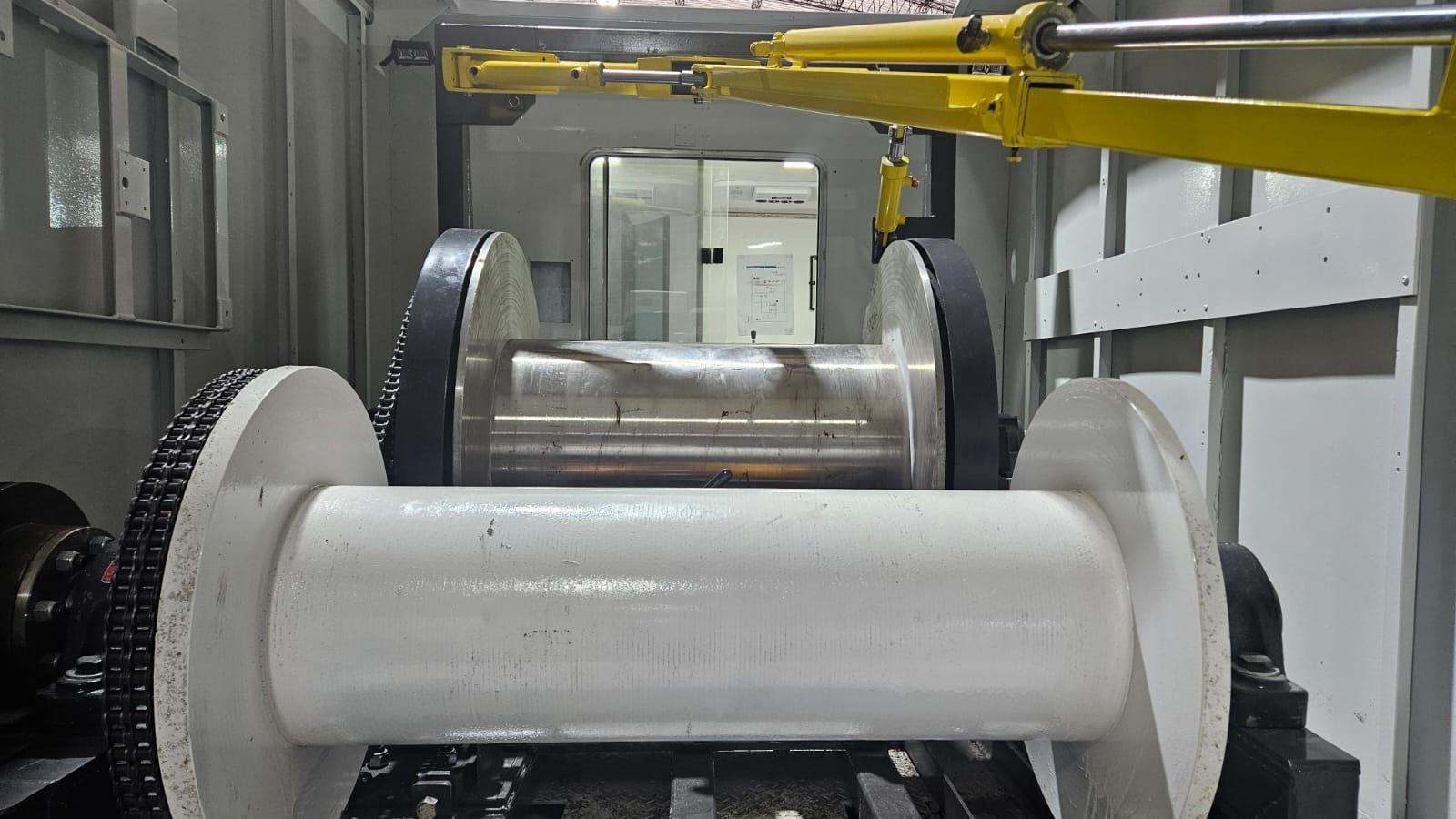 Máquina industrial con un gran rodillo blanco delante y un rodillo metálico brillante detrás en el interior de una fábrica.