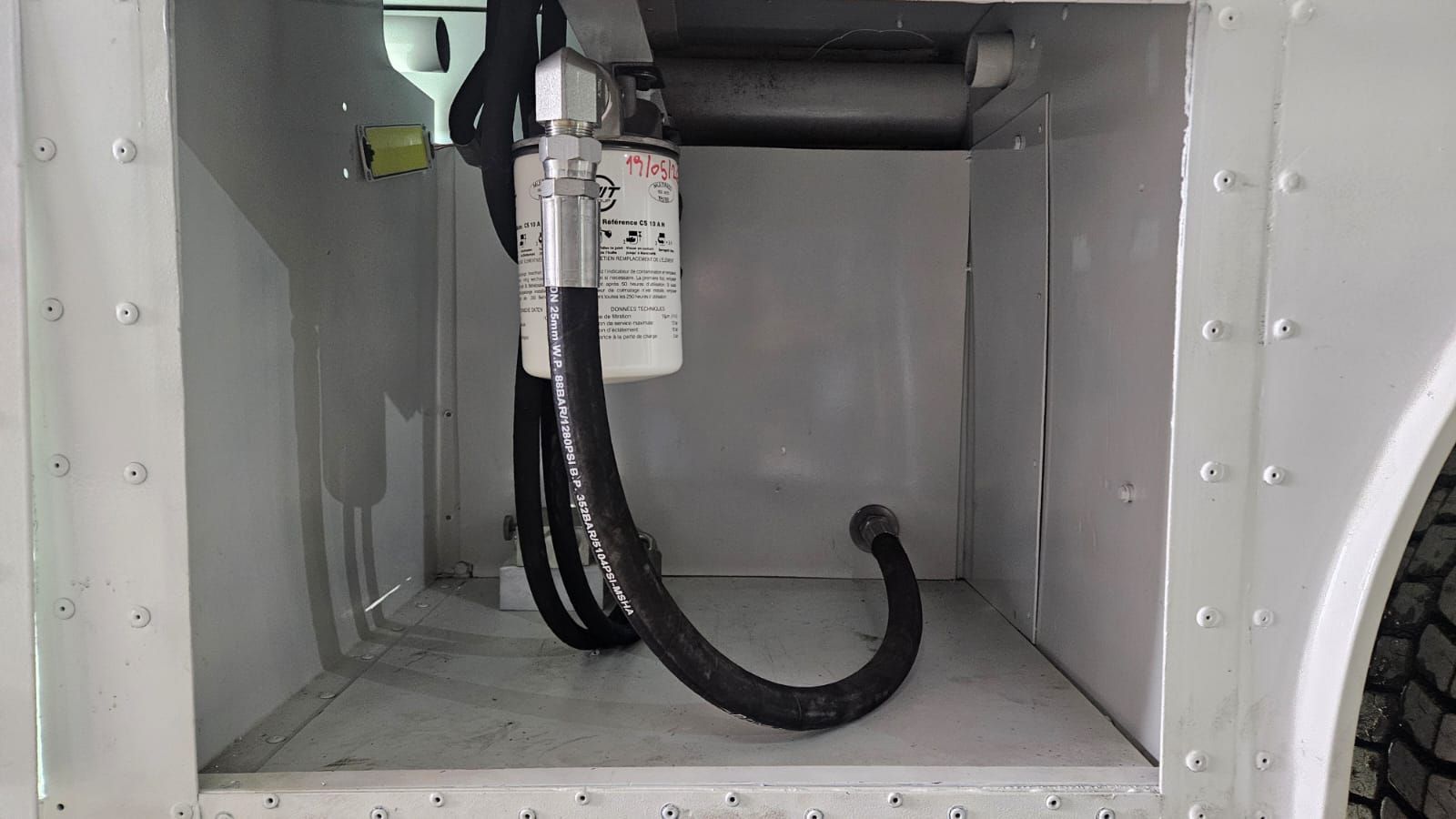 Mangueras negras y un cable dentro de un compartimento o armario de metal gris.