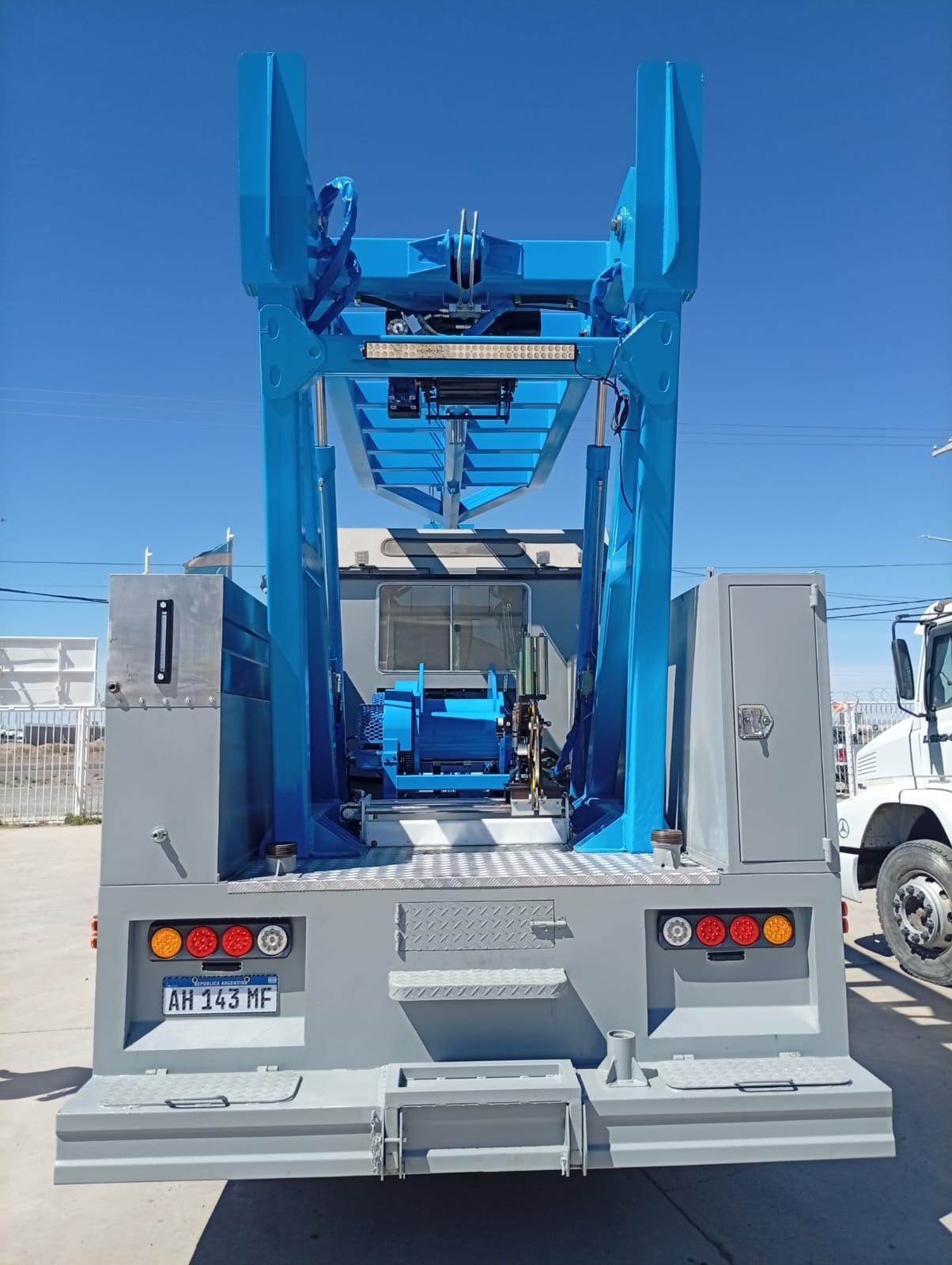 Máquina industrial azul montada sobre la plataforma de un camión, vista desde la parte trasera en un terreno al aire libre.