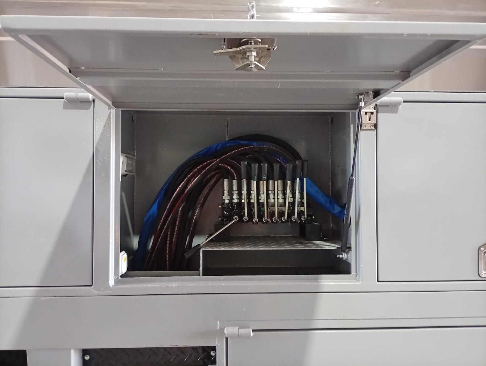 Panel eléctrico abierto con disyuntores y cableado azul dentro de un gabinete gris.