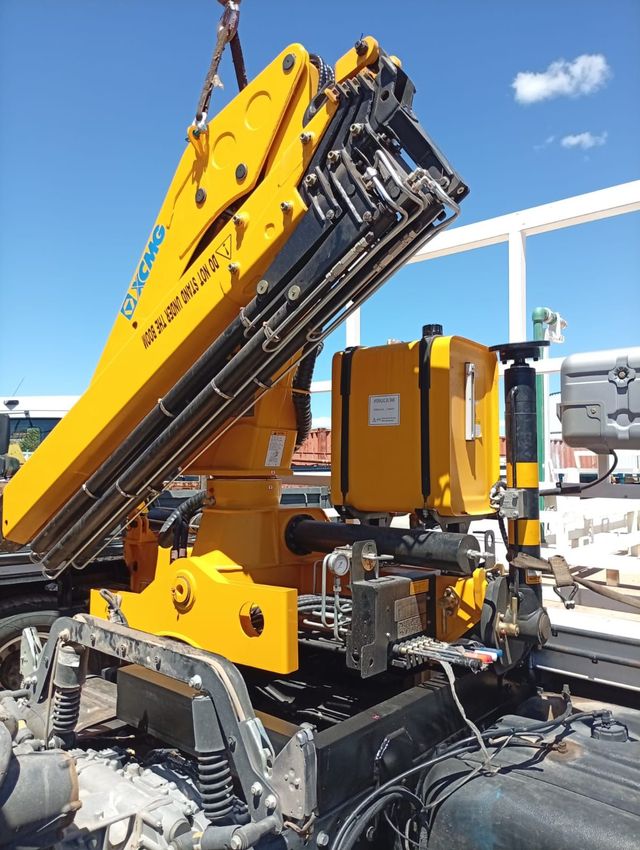 Brazo de máquina industrial amarillo con componentes hidráulicos en una obra al aire libre bajo un cielo azul.