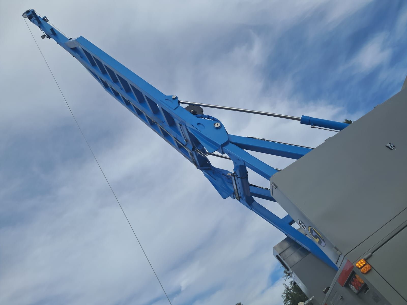 Brazo de grúa azul extendiéndose hacia el cielo nublado junto a una estructura gris.