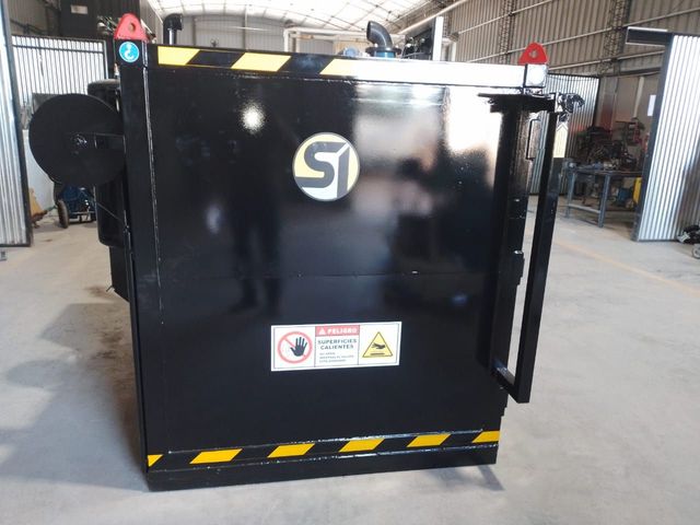 Máquina industrial negra con etiquetas de peligro en un taller, vista desde el frente.