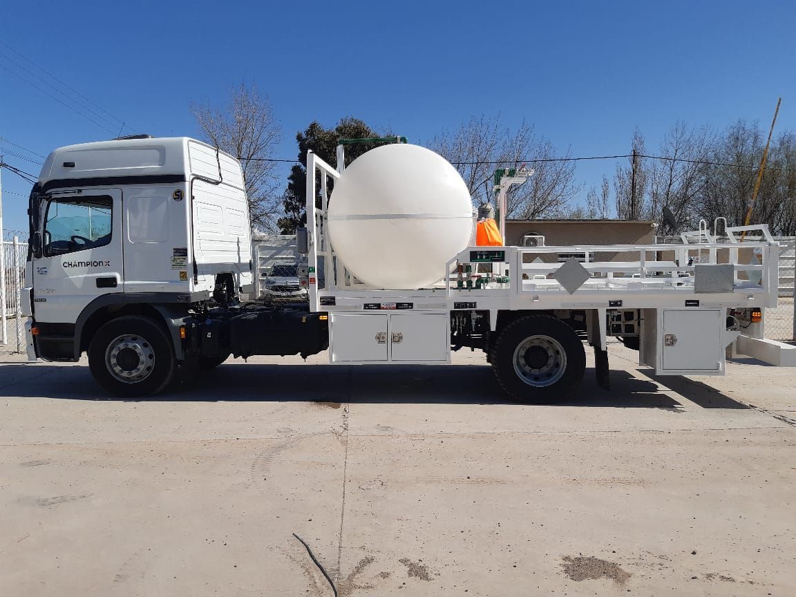Camión utilitario blanco con un gran tanque blanco estacionado al aire libre en un día soleado.