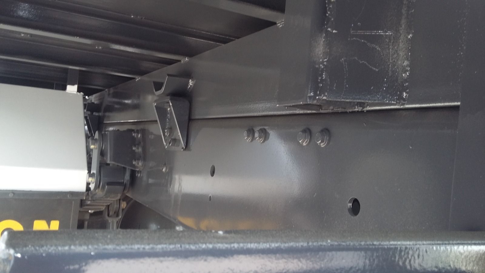 Primer plano del chasis de un vehículo de metal negro con pernos y piezas estructurales visibles.