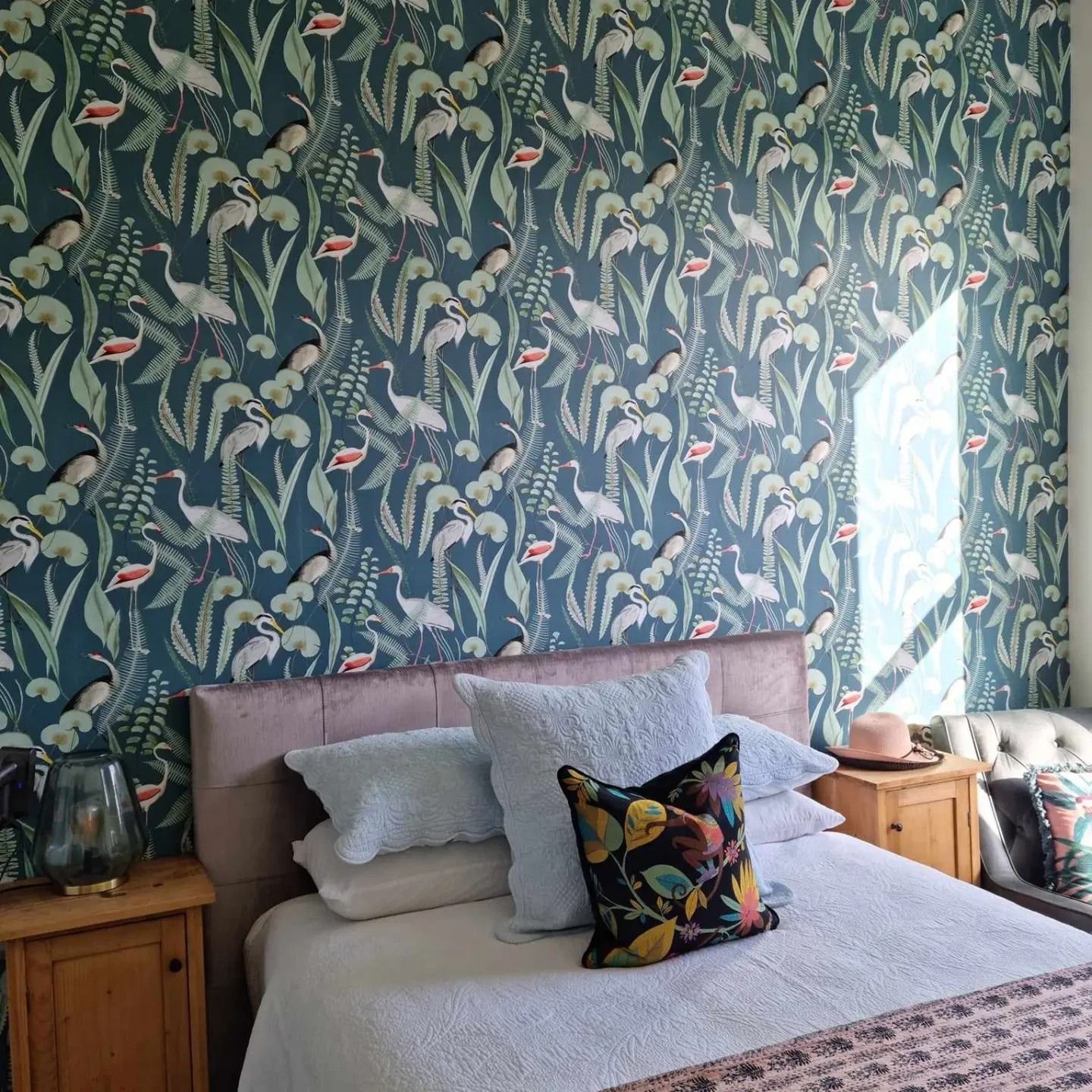 Person installs wallpaper, holding the roll to the wall. The wallpaper has a green and white leaf pattern.