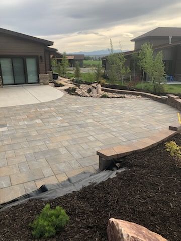 Stone patio and landscaped yard between two houses, with curved edging and distant hills.
