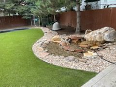 Curved gravel garden bed with large rocks and a hanging fire pit beside a green lawn
