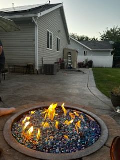 Backyard fire pit with colorful glass flames beside a concrete patio and gray house