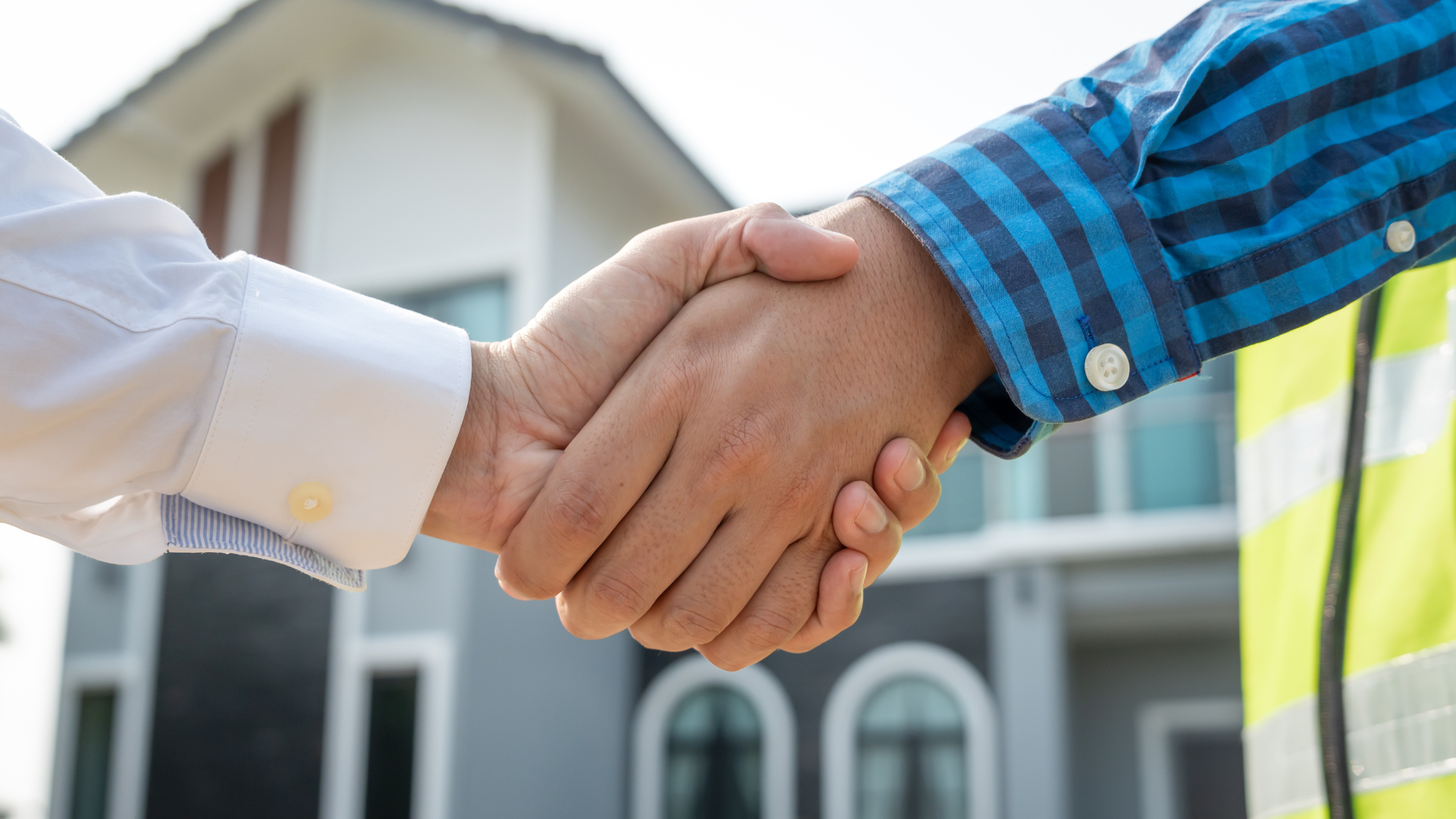 Two people shaking hands in front of a house. One wears a blue striped shirt and the other wears a white shirt.