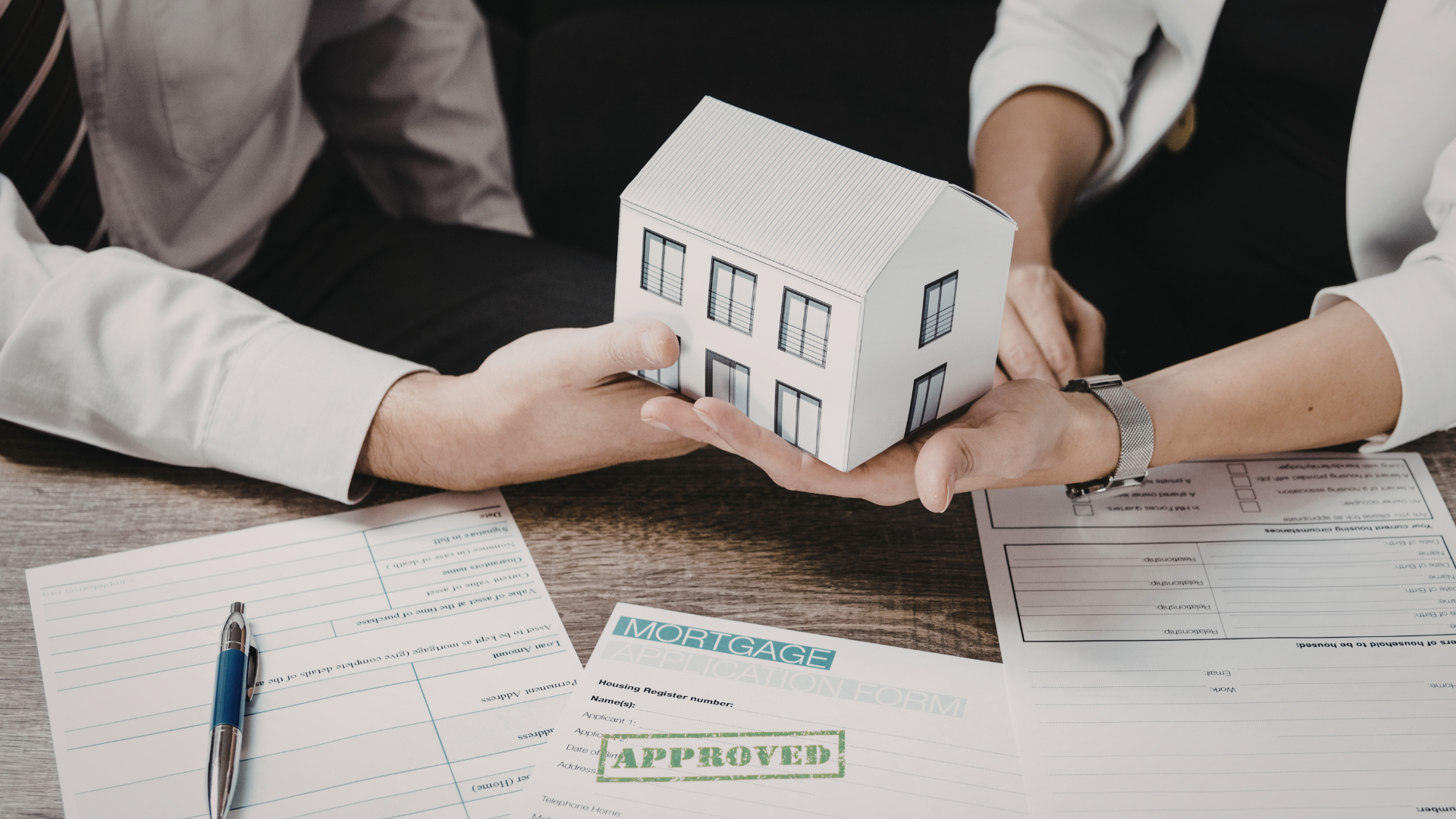 Hands holding a model house above paperwork, with an 