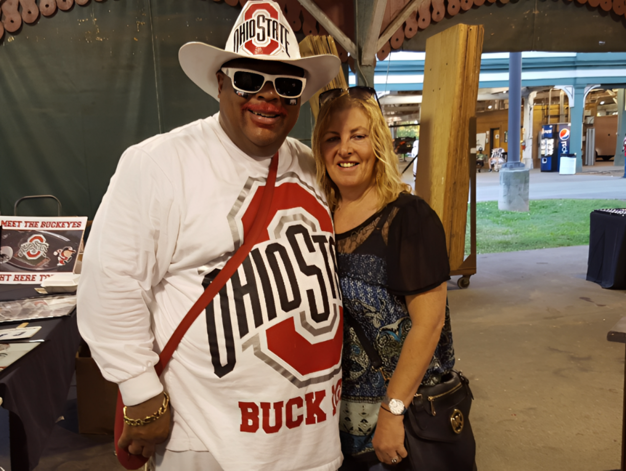 A person in an Ohio State hat and shirt posing for a photo with a smiling person in a blue patterned top at an event.