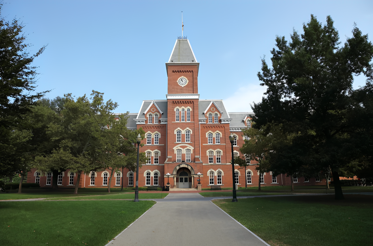 University Hall, a historic red brick building with a central clock tower, surrounded by trees and a green lawn.