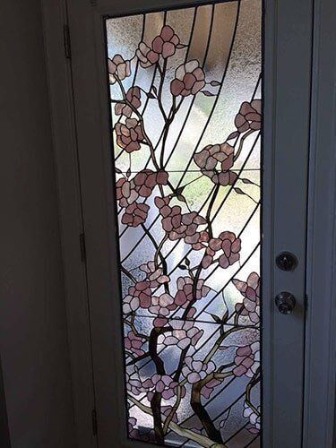 Stained-glass door panel with flowering pink tree branches. Brown and black stems, light background.