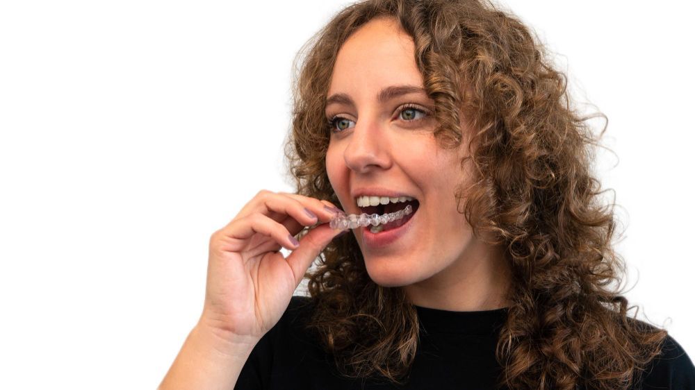 Woman with curly hair inserting clear aligner into mouth.
