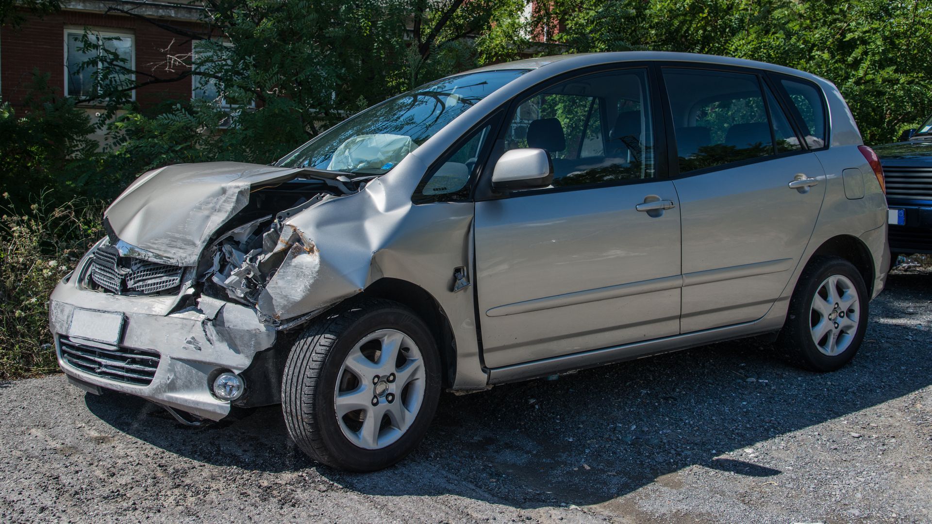 Totaled silver car parked on gravel and ready to be sold for parts