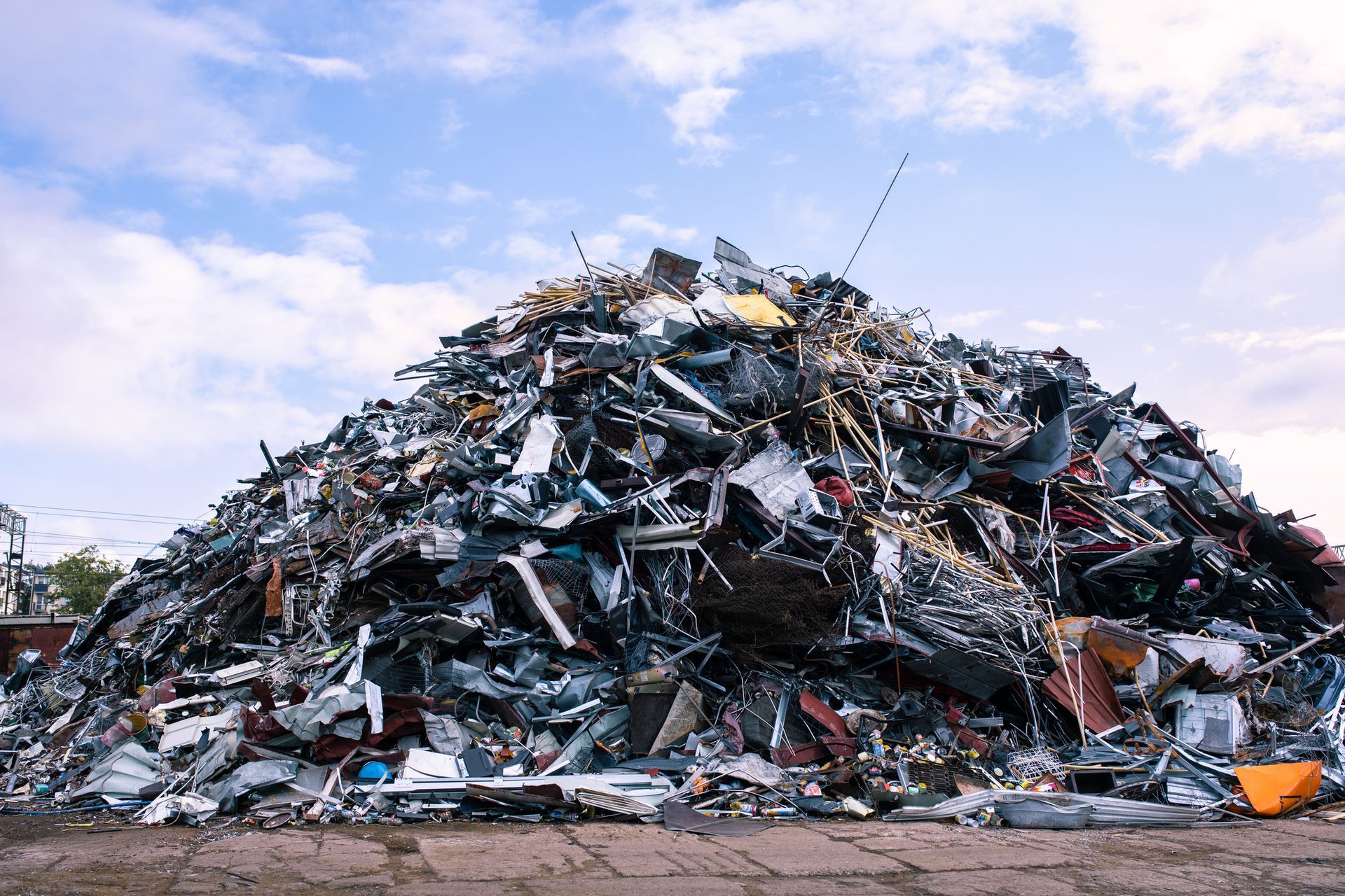 Towering mountain of scrap metal at a junkyard showcases the essence of recycling under a blue sky.