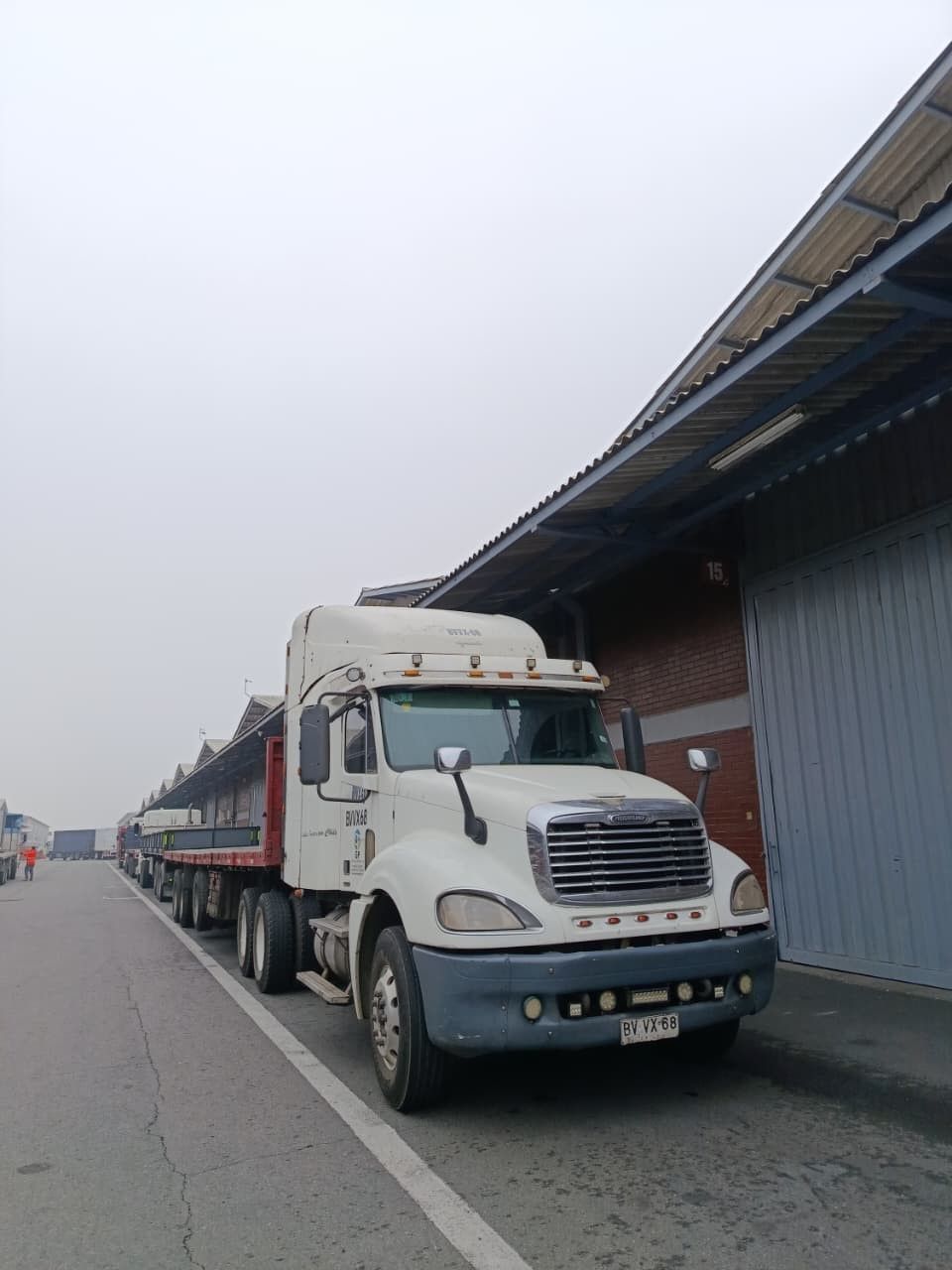 Un camión semirremolque blanco estacionado junto a un almacén en una calle industrial.