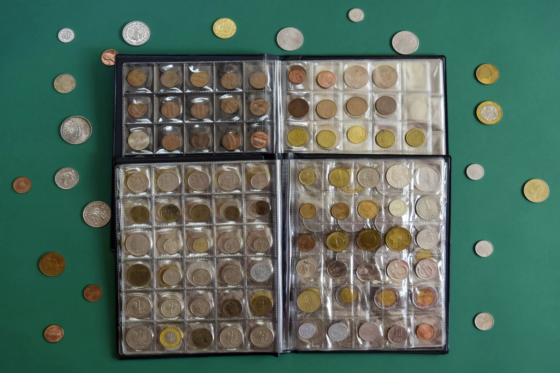 Assorted coins arranged in four clear trays on a green surface, with loose coins scattered around them