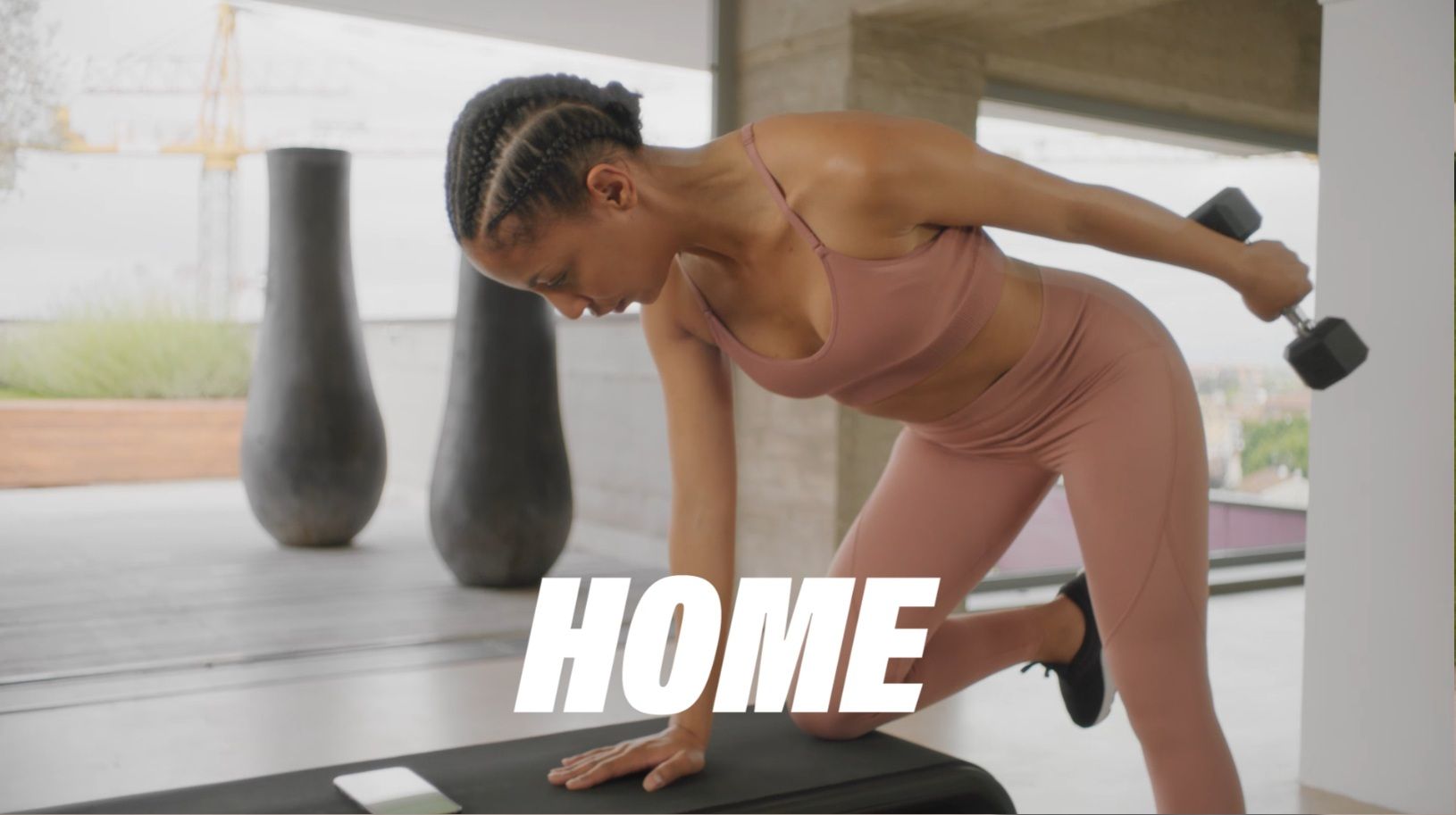 A person in workout gear performs a tricep kickback with a dumbbell while leaning on a bench in a gym setting.