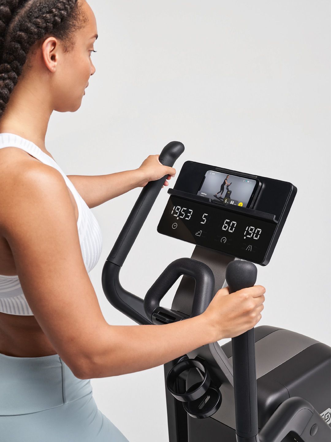 A person holding the handles of a black elliptical machine, focusing on the digital console showing workout metrics.