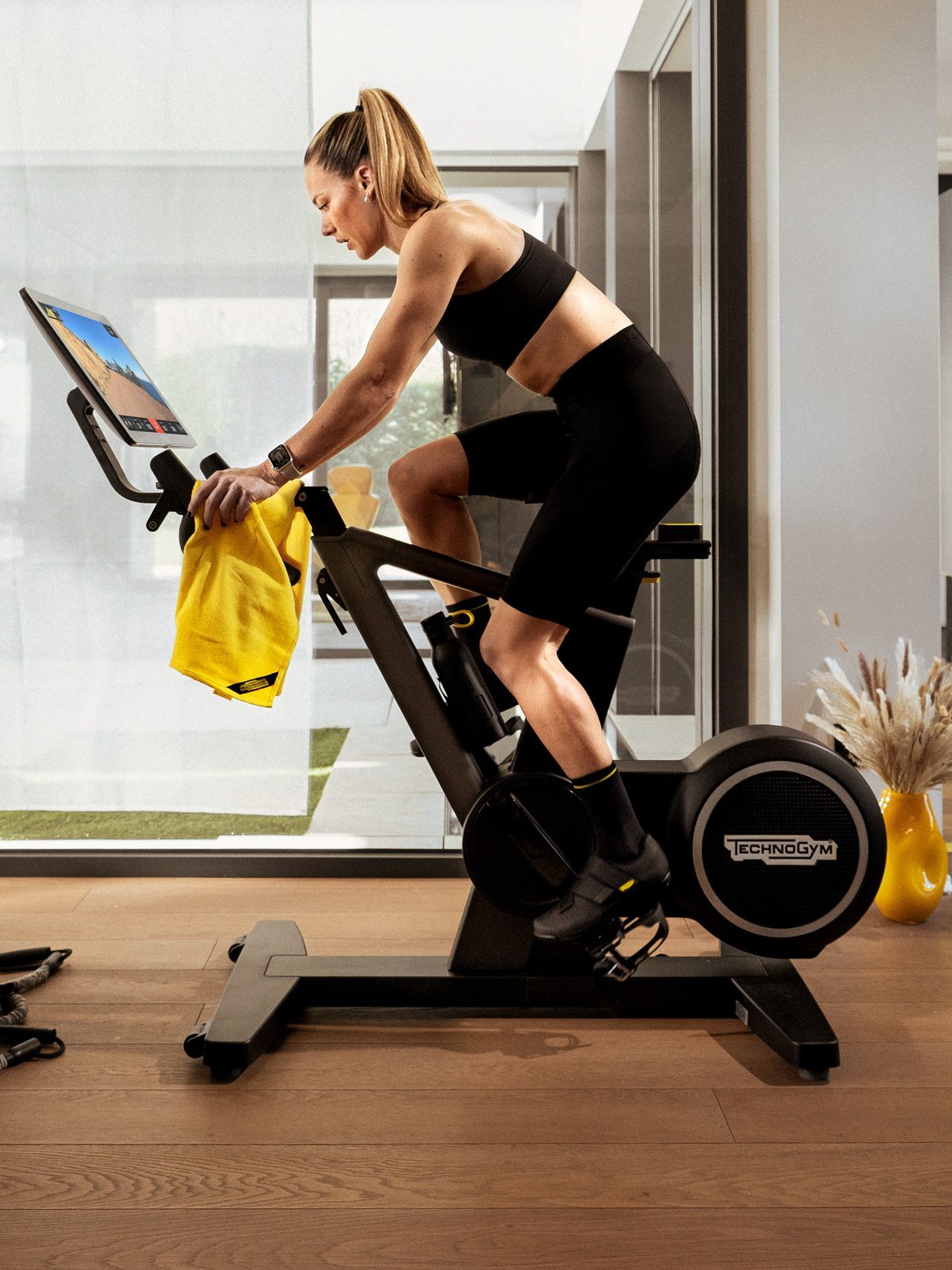 A person in athletic gear works out on a Technogym stationary bike in a modern, sunlit room.
