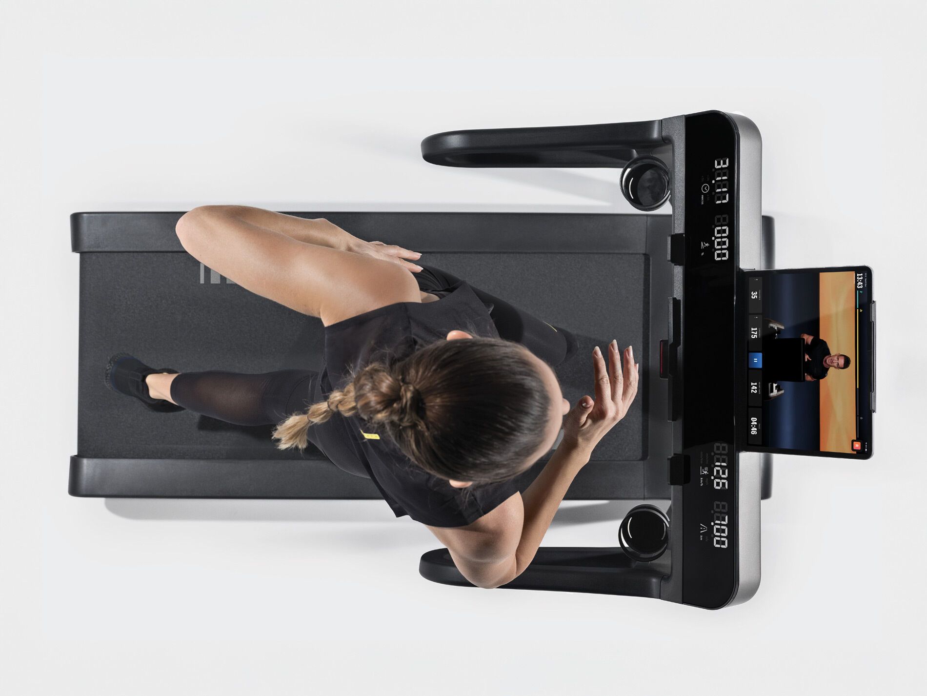A person jogging on a black treadmill, viewed from above, with a digital screen displaying a workout program.