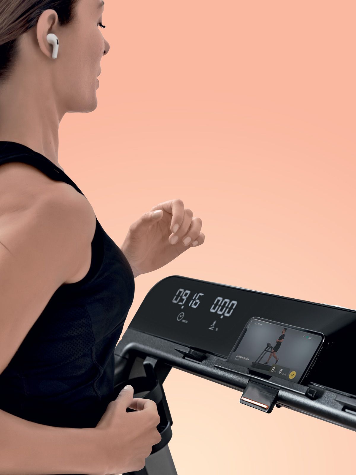 A person wearing wireless earbuds runs on a treadmill, looking toward the digital display and phone mount.
