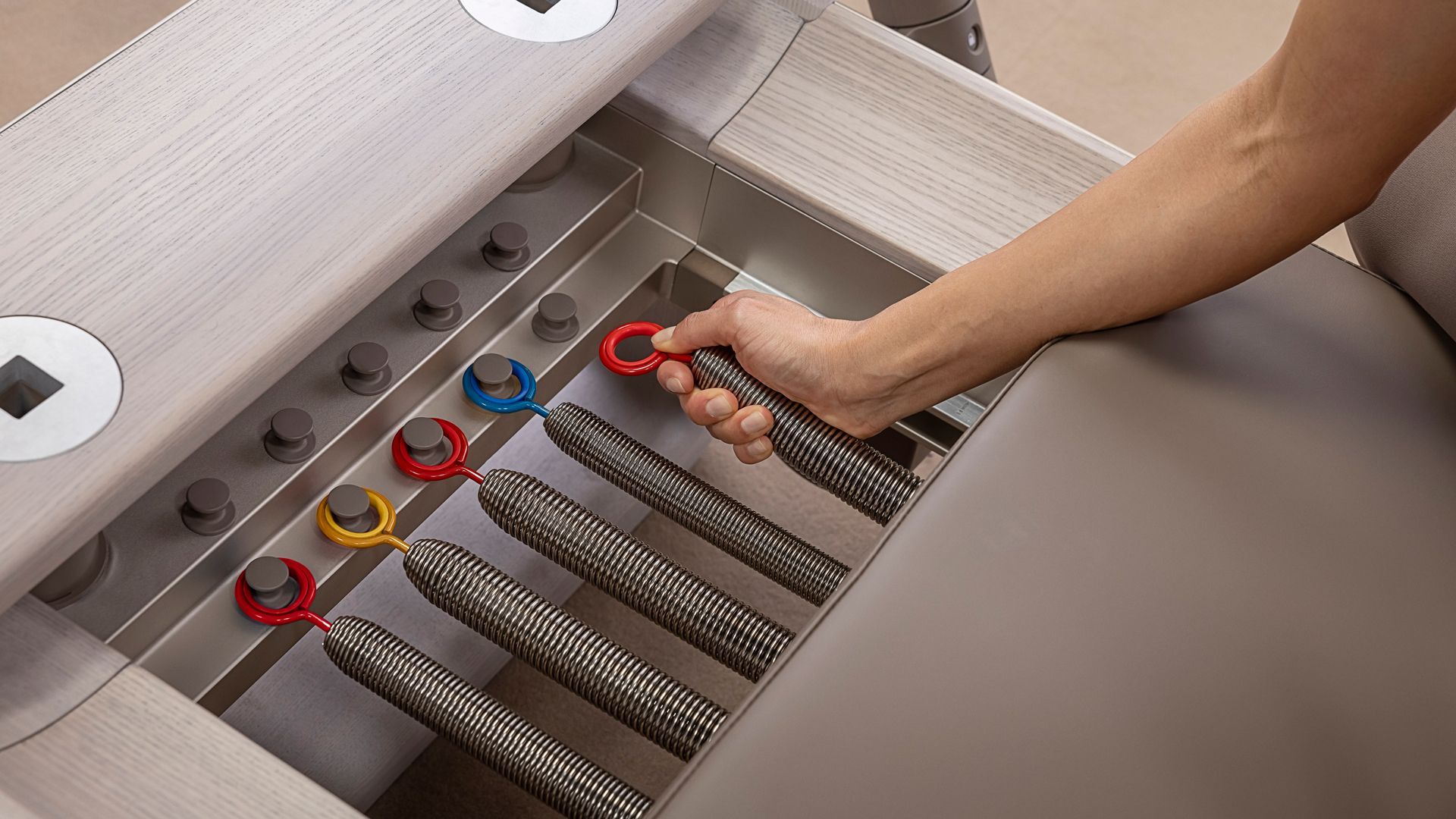 A person’s hand adjusts colorful resistance springs on a Pilates reformer machine.