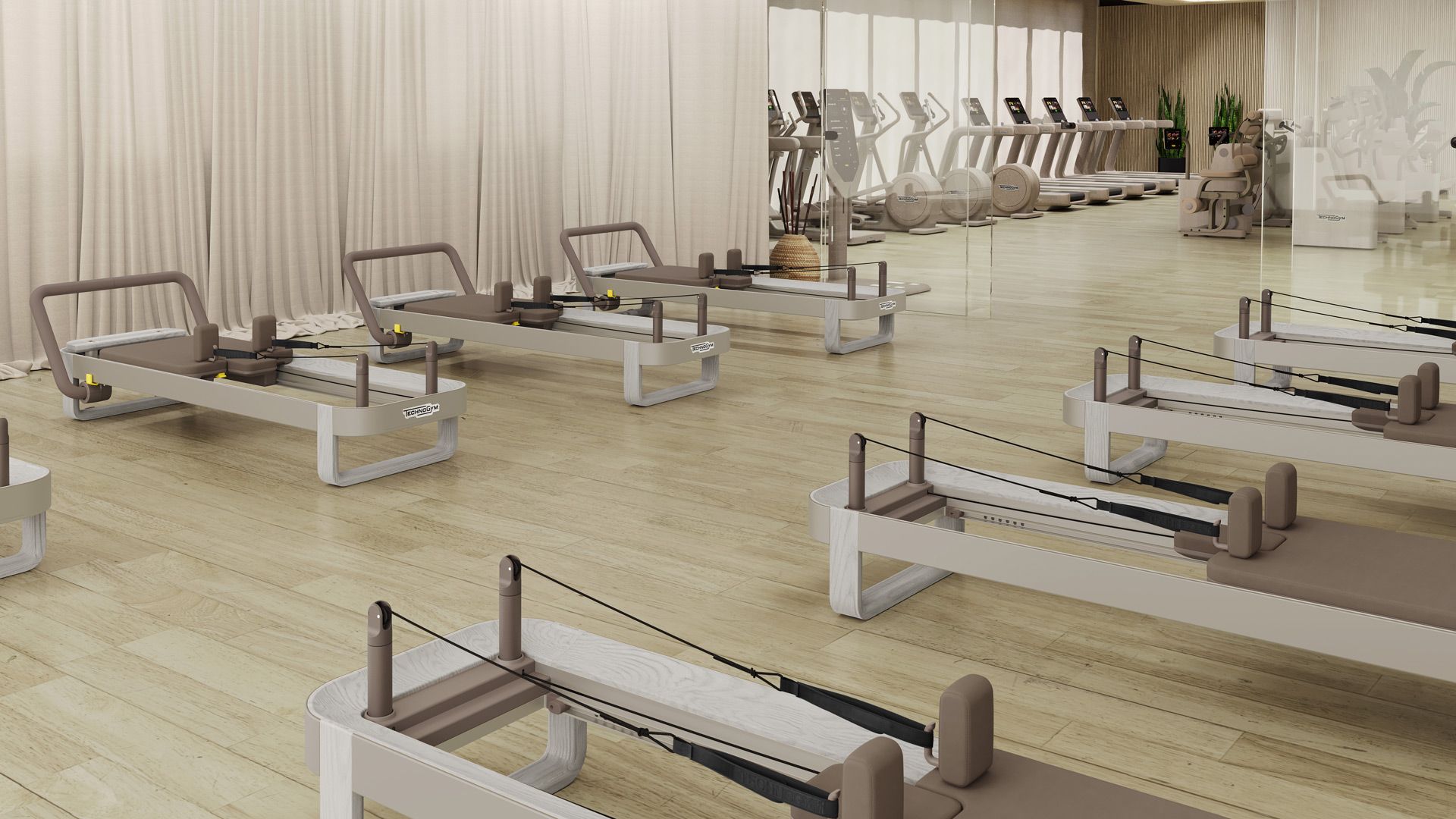 A bright, airy Pilates studio featuring several light-colored reformer machines on a wooden floor.
