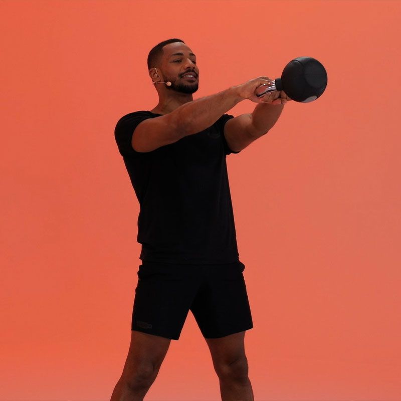 A person in black athletic wear performs a kettlebell swing in front of a solid orange background.