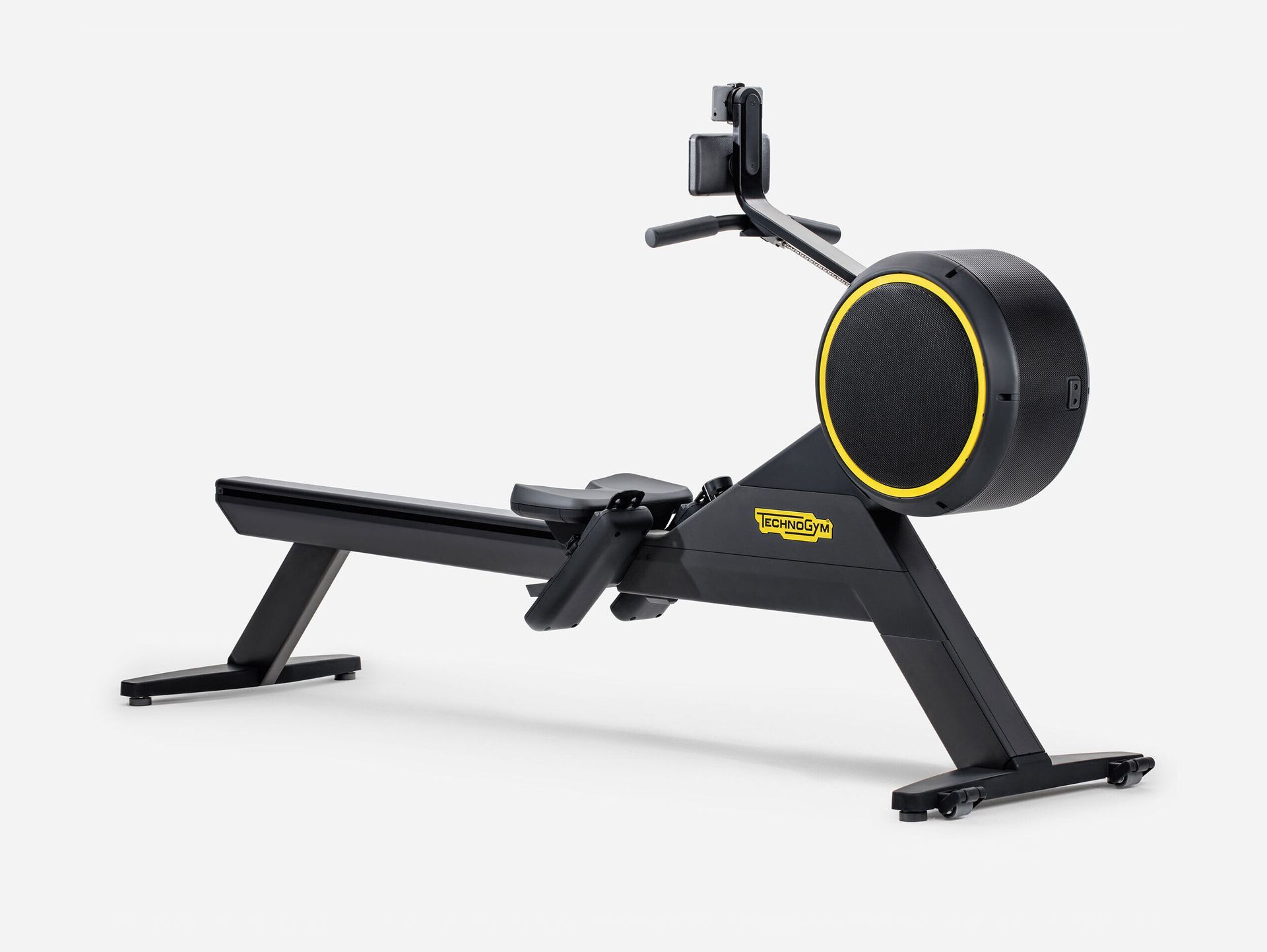 A black Technogym indoor rowing machine with yellow accents set against a plain light gray background.