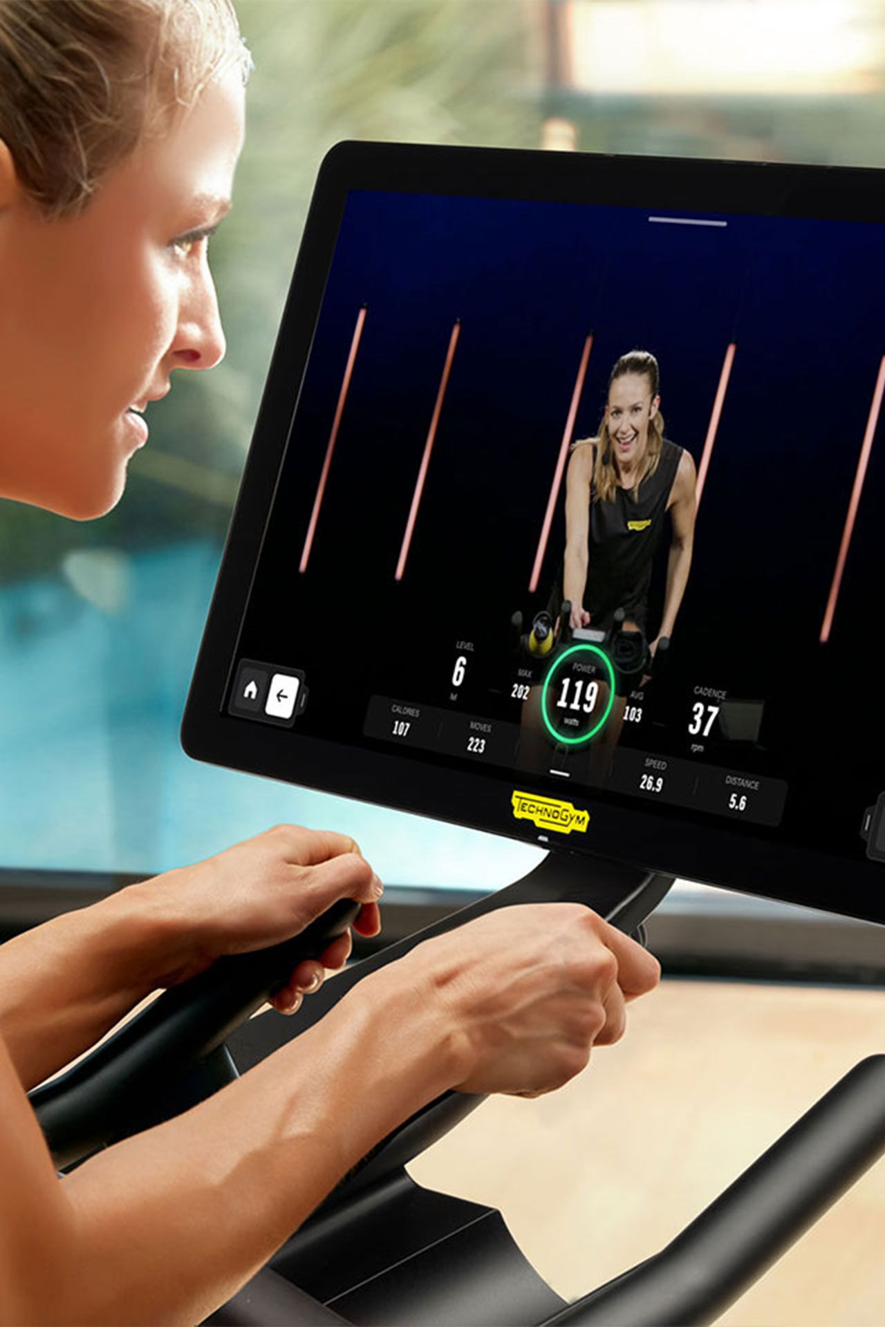 A person exercising on a stationary bike while viewing a live cycling class on a mounted screen.