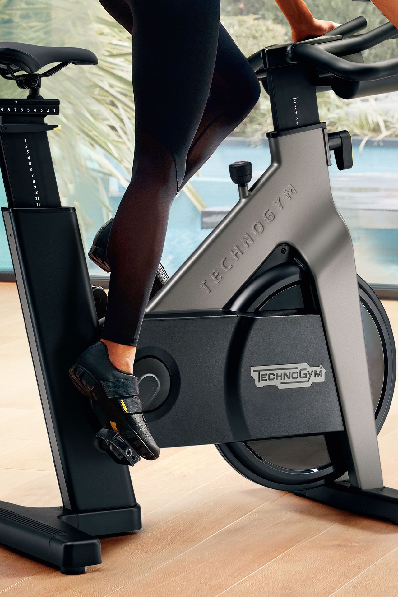 A person in black leggings cycles on a Technogym stationary bike indoors.