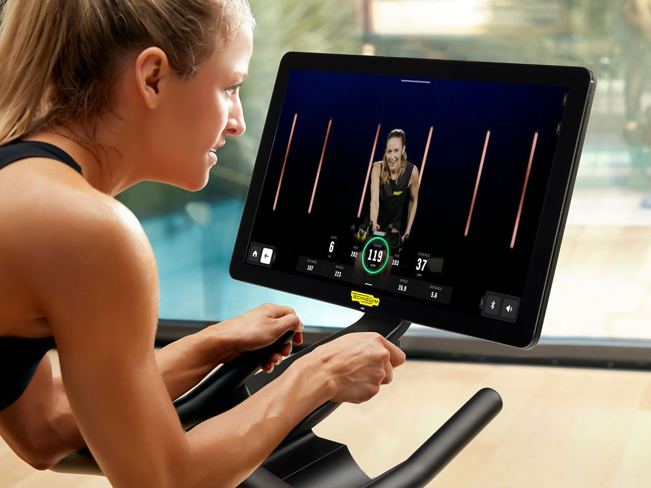A person riding a stationary bike, following a digital workout class on a mounted screen.