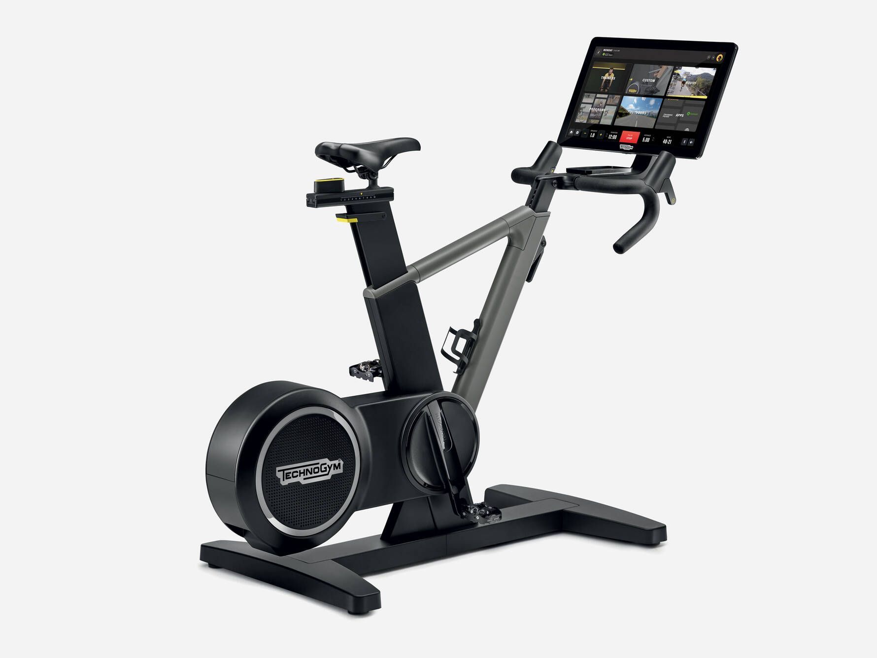 A Technogym stationary exercise bike with a black frame, flywheel, and integrated tablet display on the handlebars.