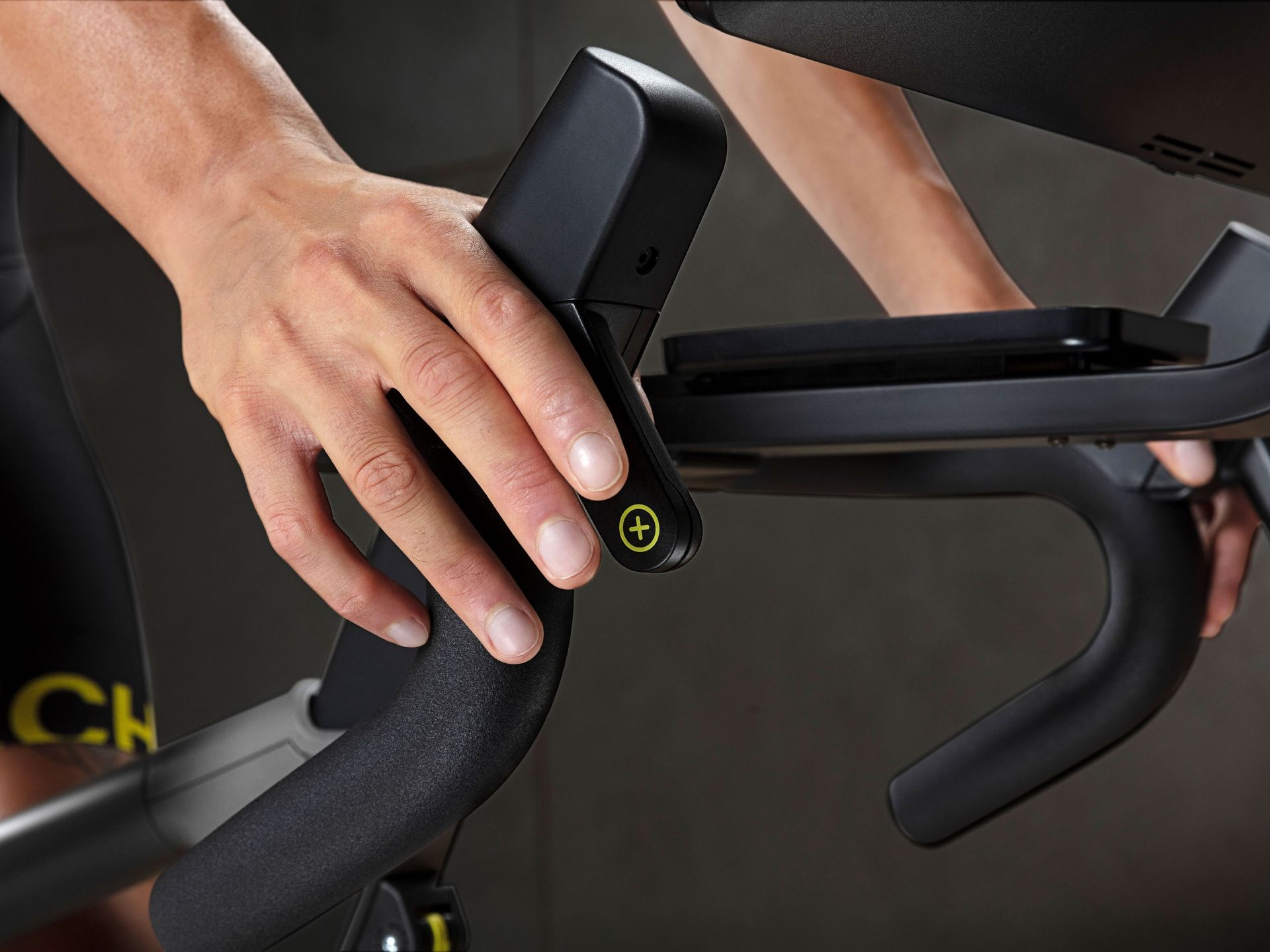 A hand adjusts the resistance dial on a black exercise bike handlebar during a workout.