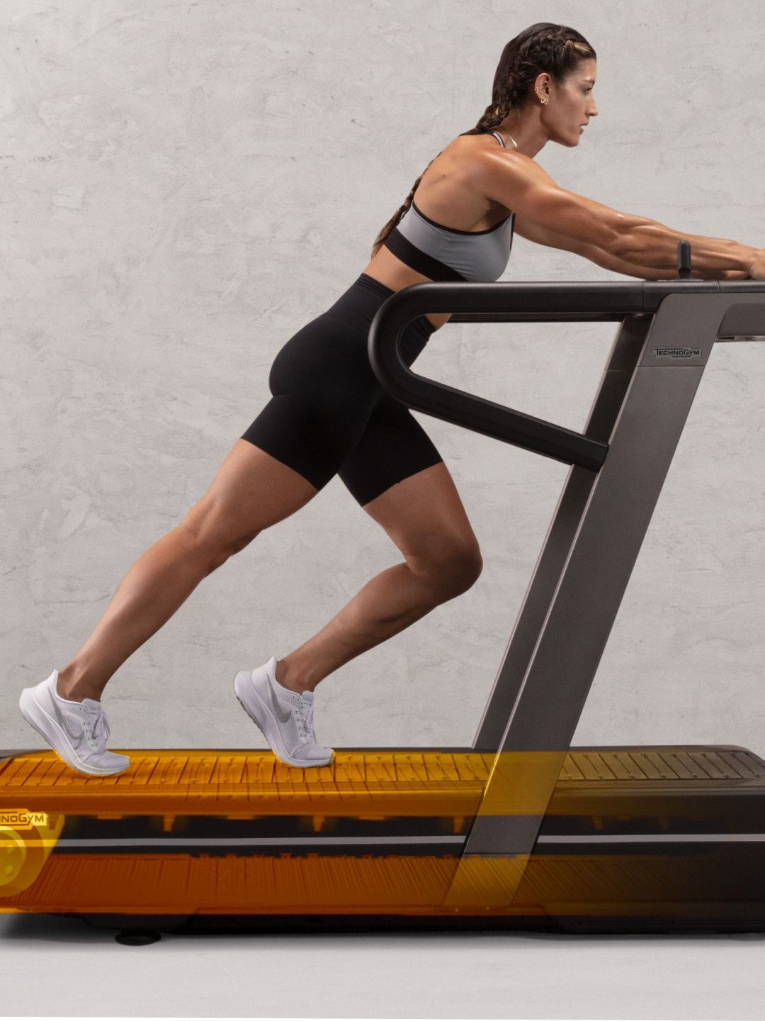 A person in workout gear performs a pushing exercise on a treadmill against a neutral background.