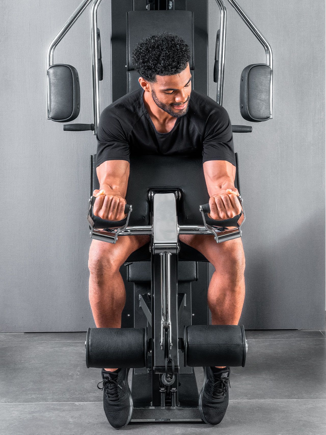 A person performing seated bicep curls on a gym machine, wearing a black shirt and athletic shoes.