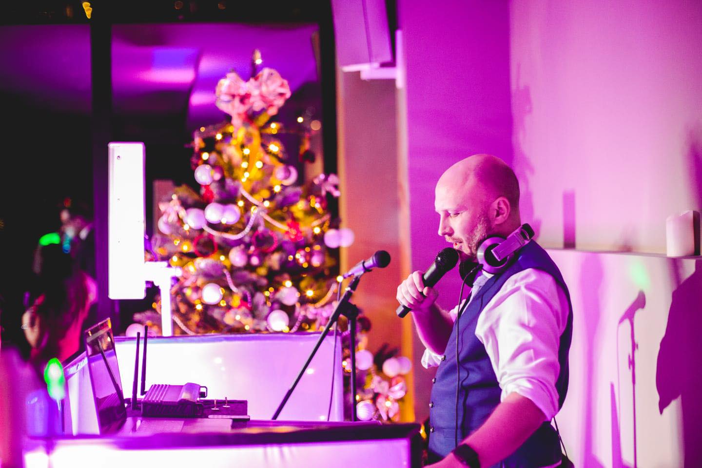 A dj is playing music and singing into a microphone in front of a christmas tree.
