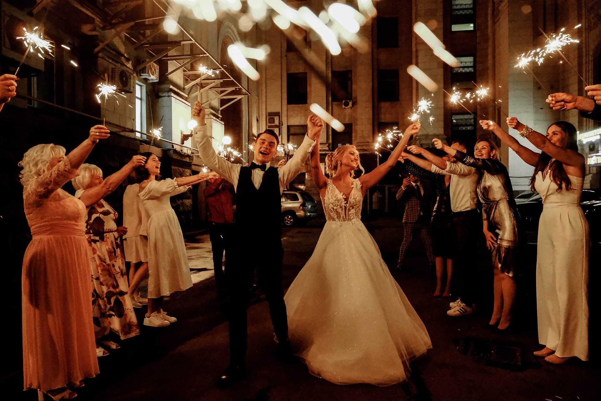 A bride and groom are walking through a crowd of people holding sparklers.