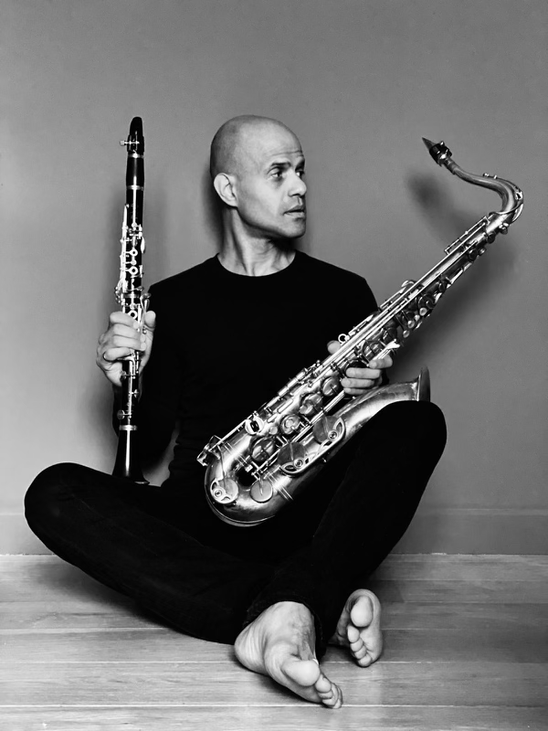 A man is sitting on the floor holding a saxophone and a clarinet