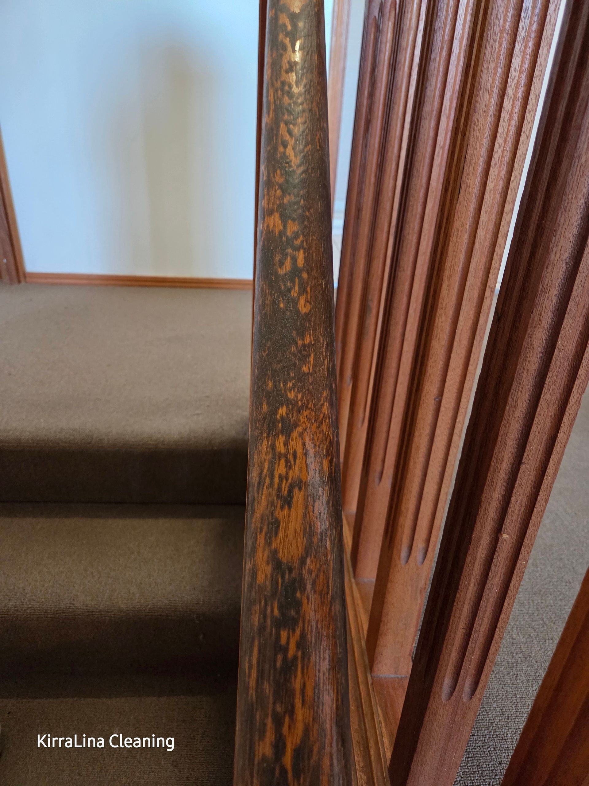 Close-Up of A Wooden Stair Railing with Worn, Peeling Finish. Carpeted Stairs Lead Upwards — KirraLina Cleaning Services in Tweed Heads, NSW