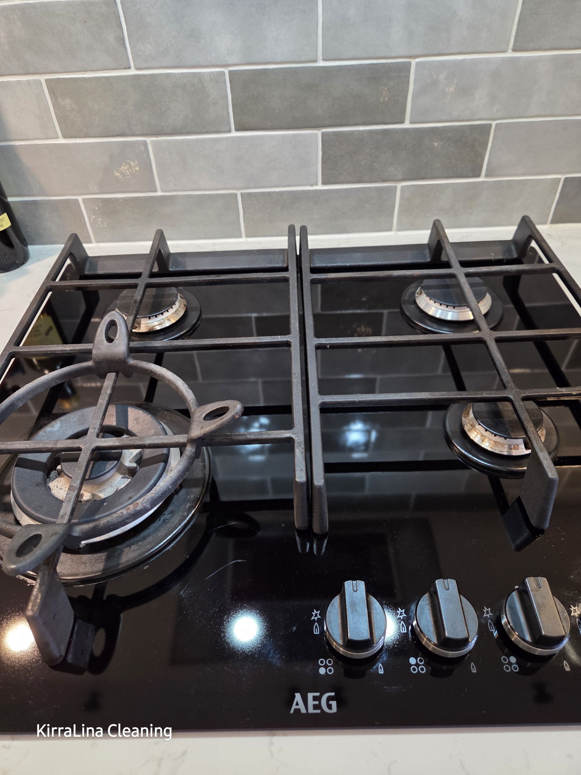 Black Glass Aeg Gas Stovetop With Four Burners and Cast-iron Grates in a Tiled Kitchen — KirraLina Cleaning Services in Tweed Heads, NSW
