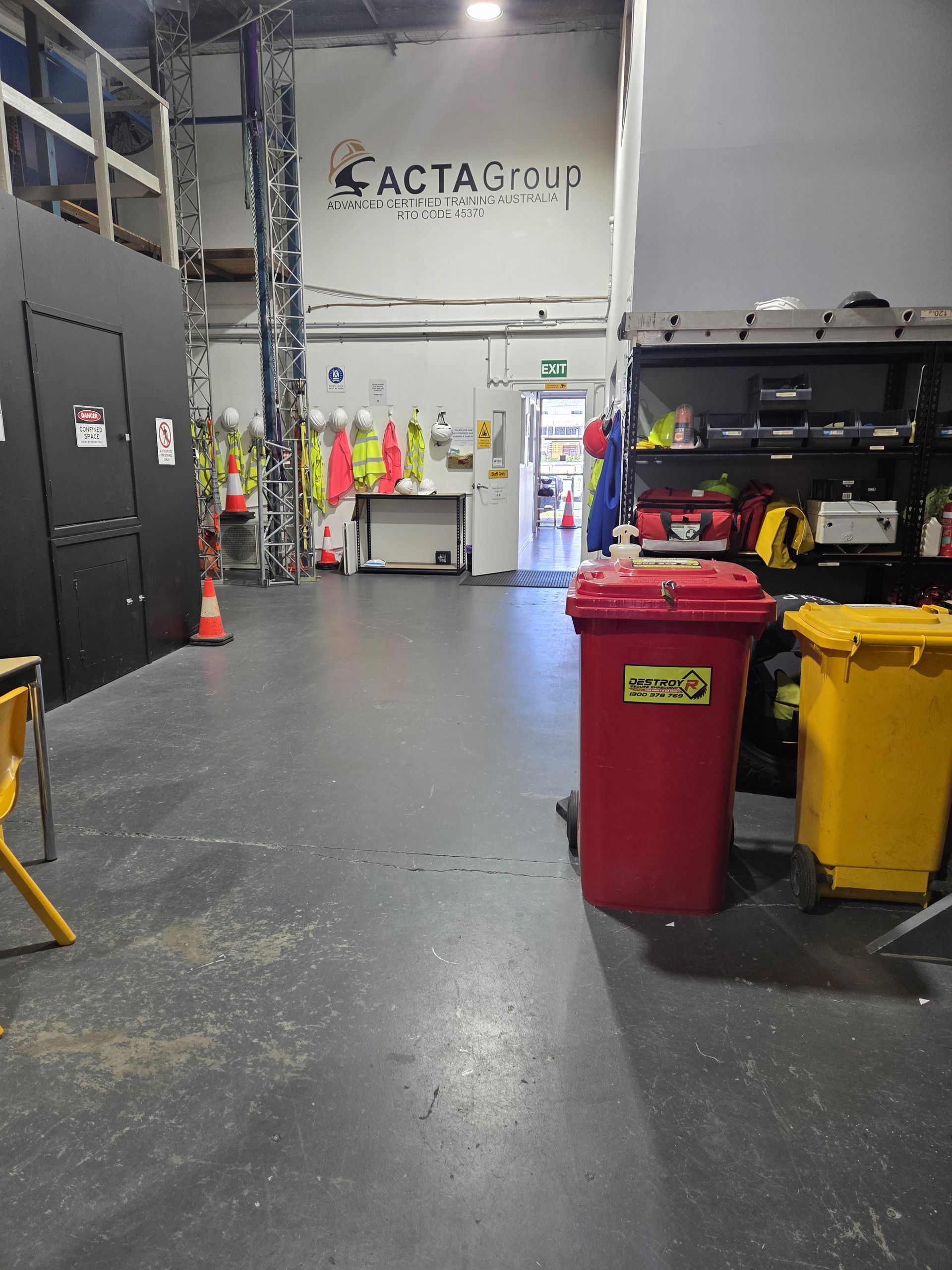 Industrial workshop with cabinets, safety gear, and red and yellow trash bins on a concrete floor.