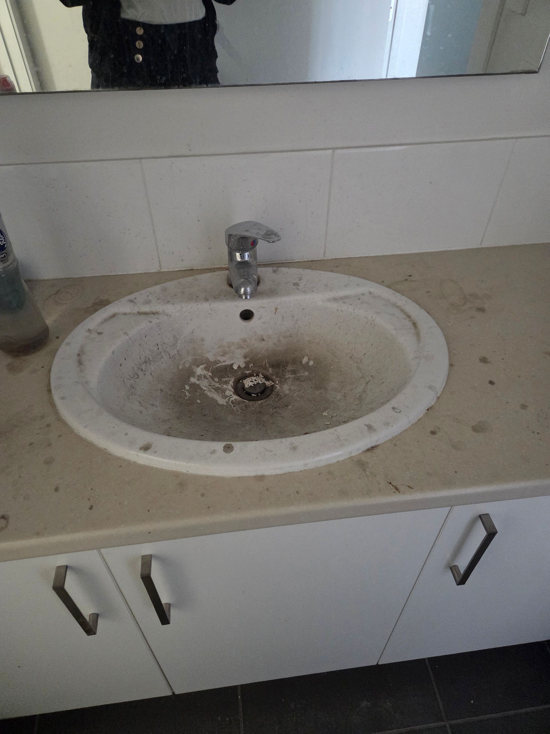Dirty Bathroom Sink with Speckled Countertop and Mirror Above — KirraLina Cleaning Services in Tweed Heads, NSW