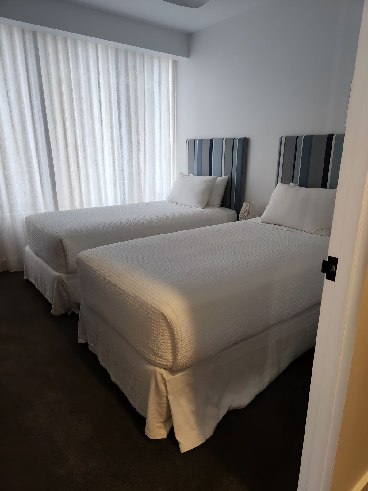 Two twin beds with white bedding in a room with a window and white curtains.